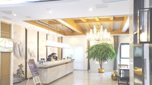 A modern hotel lobby with a reception desk, a large chandelier, a potted plant, and a seating area. - Haolilai Garden Hotel (Sanming)