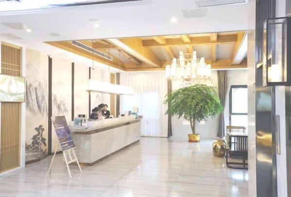 A modern hotel lobby with a reception desk, a large chandelier, a potted plant, and a seating area. - Haolilai Garden Hotel (Sanming)