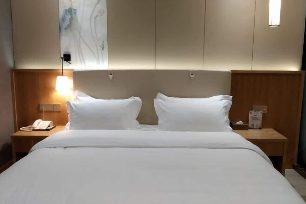 Una habitación de hotel con una cama, dos mesitas de noche, una lámpara y un cuadro en la pared.