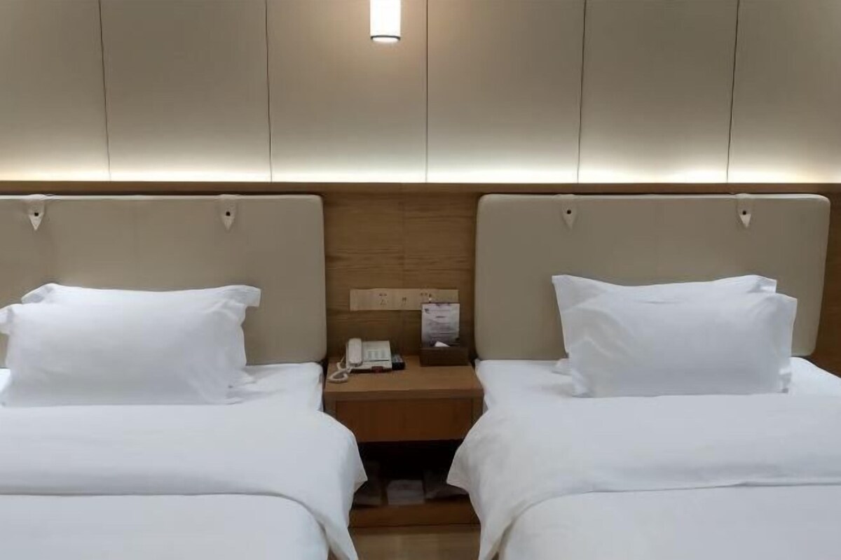 A hotel room with two beds, a wooden headboard, a bedside table with a phone, and a small nightstand.