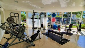 Een sportschool met diverse trainingsapparaten, waaronder krachtapparaten en losse gewichten, en grote ramen met uitzicht op het omliggende landschap.
