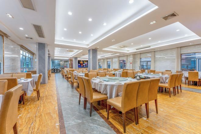 A spacious banquet hall with round tables and chairs, large windows, and a polished wooden floor.