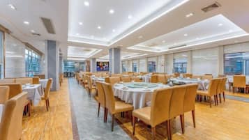 Un amplio salón de banquetes con mesas y sillas redondas, ventanas grandes y un piso de madera pulida.