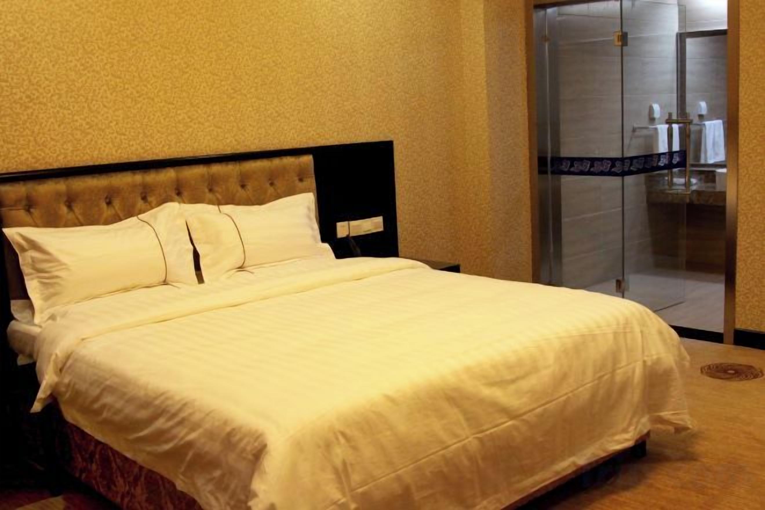 A hotel room with a bed, a glass shower enclosure, and a visible bathroom.