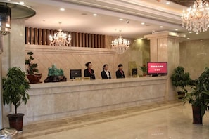 A hotel reception desk with a TV screen, four staff members, and decorative plants.