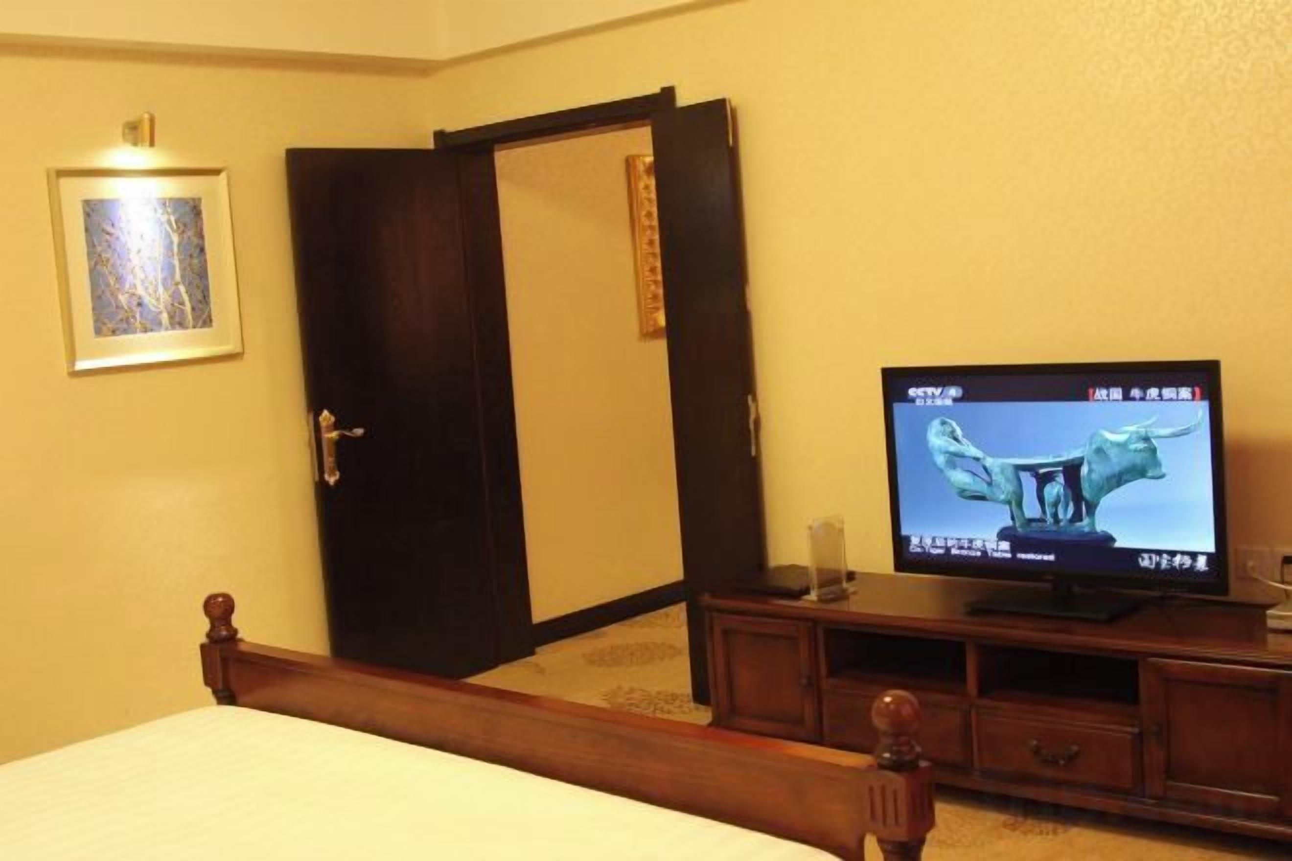 Habitación de hotel con cama, televisor, armario y un cuadro en la pared.