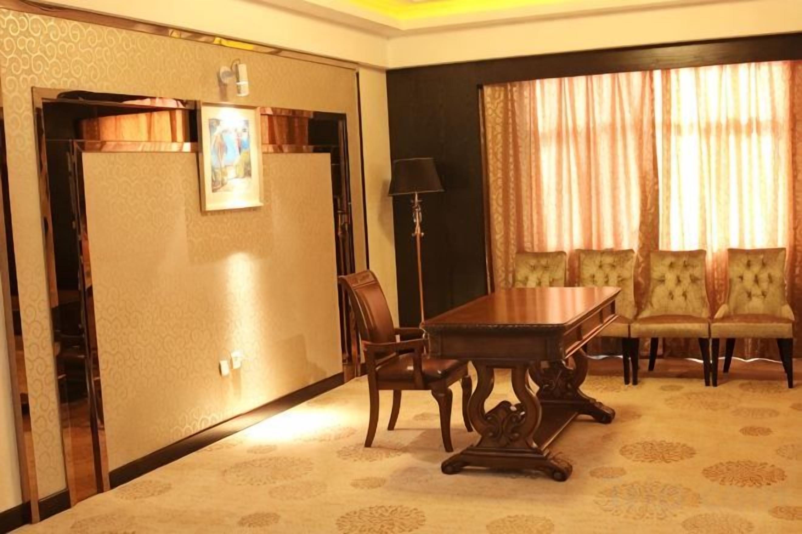 A hotel room with a dining table, four chairs, a sofa, a lamp, and a window with curtains.
