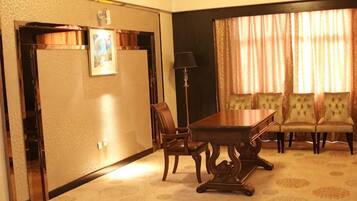 A hotel room with a dining table, four chairs, a sofa, a lamp, and a window with curtains.