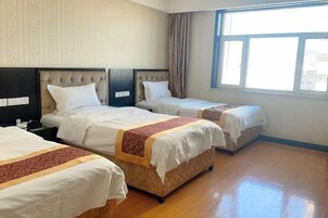 Habitación de hotel con tres camas, un ventanal grande y suelo de madera.