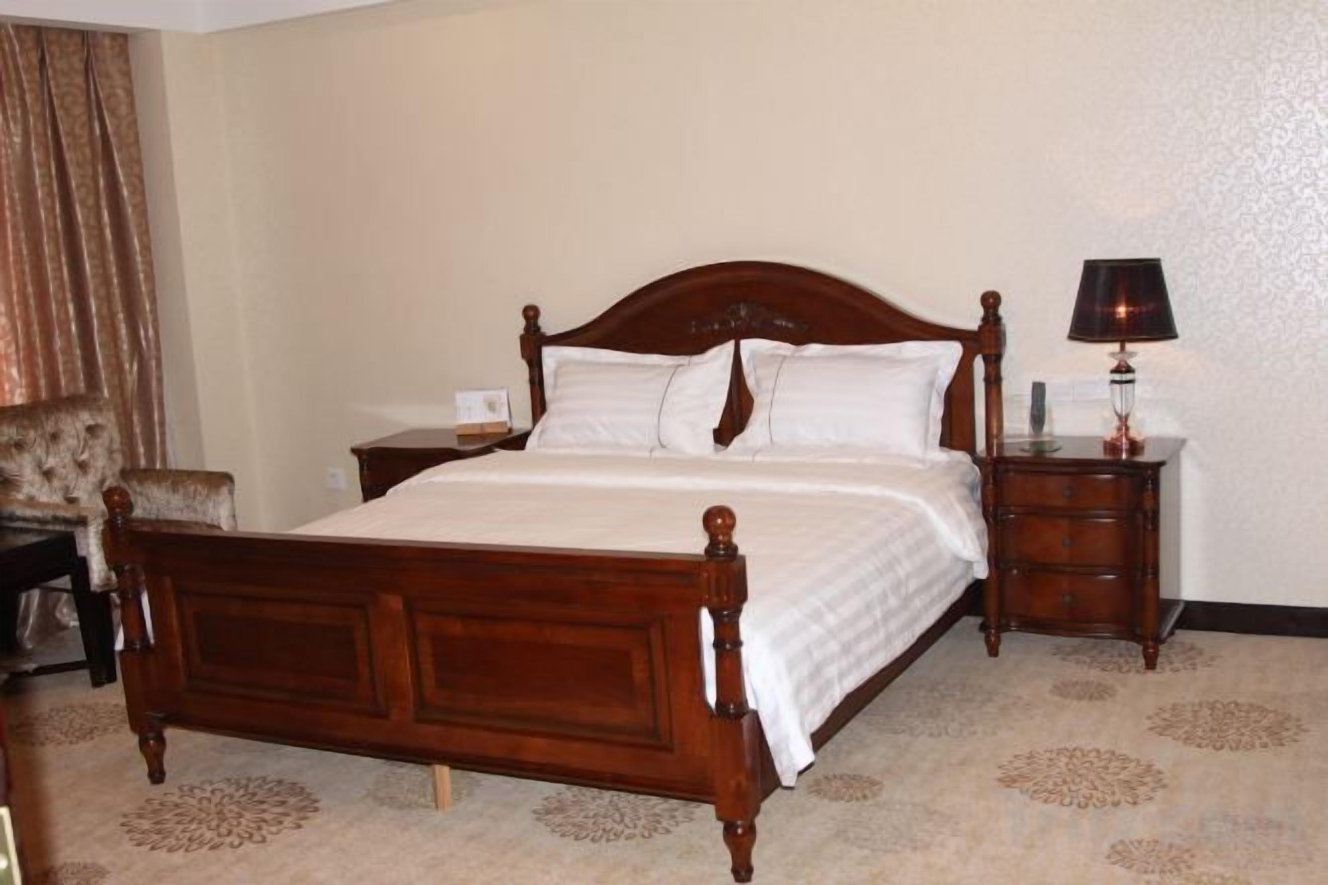 A standard hotel room with a wooden bed, a nightstand, a lamp, and a chair.