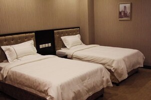 Habitación de hotel con dos camas individuales, cada una con cabecera y ropa de cama blanca.