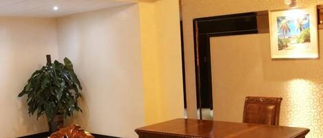 A hotel room with a wooden dining table, a potted plant, and a framed picture on the wall.