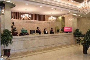 A hotel reception area with a marble counter, receptionists, a television, and potted plants. - Lanyi Holiday Hotel (Kelan)