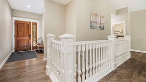 A hallway with a wooden door, white railing, and a bench.