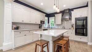 A modern kitchen with white cabinetry, a central island, wooden stools, and a black oven.