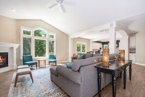Ein geräumiges Wohnzimmer mit Kamin, großen Fenstern, einer Couch und einem Esstisch.