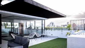 A modern rooftop terrace with glass walls, outdoor seating, and a view of the city skyline. - Lovely 2BR Spacious and Centric Apt. - Renty 501 (Santo Domingo)