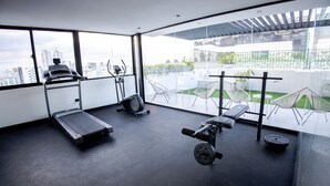 A modern gym with a treadmill, stationary bike, and weight bench. - Lovely 2BR Spacious and Centric Apt. - Renty 501 (Santo Domingo)