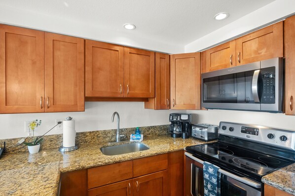 A kitchen with wooden cabinets, a stainless steel microwave, a stove, and a coffee maker.