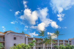 A hotel with a name sign, multiple balconies, and palm trees.