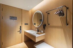 A modern bathroom with a wooden vanity, a mirror with a circular frame, a towel rack, and a shower area. - Ji Hotel (Korla)