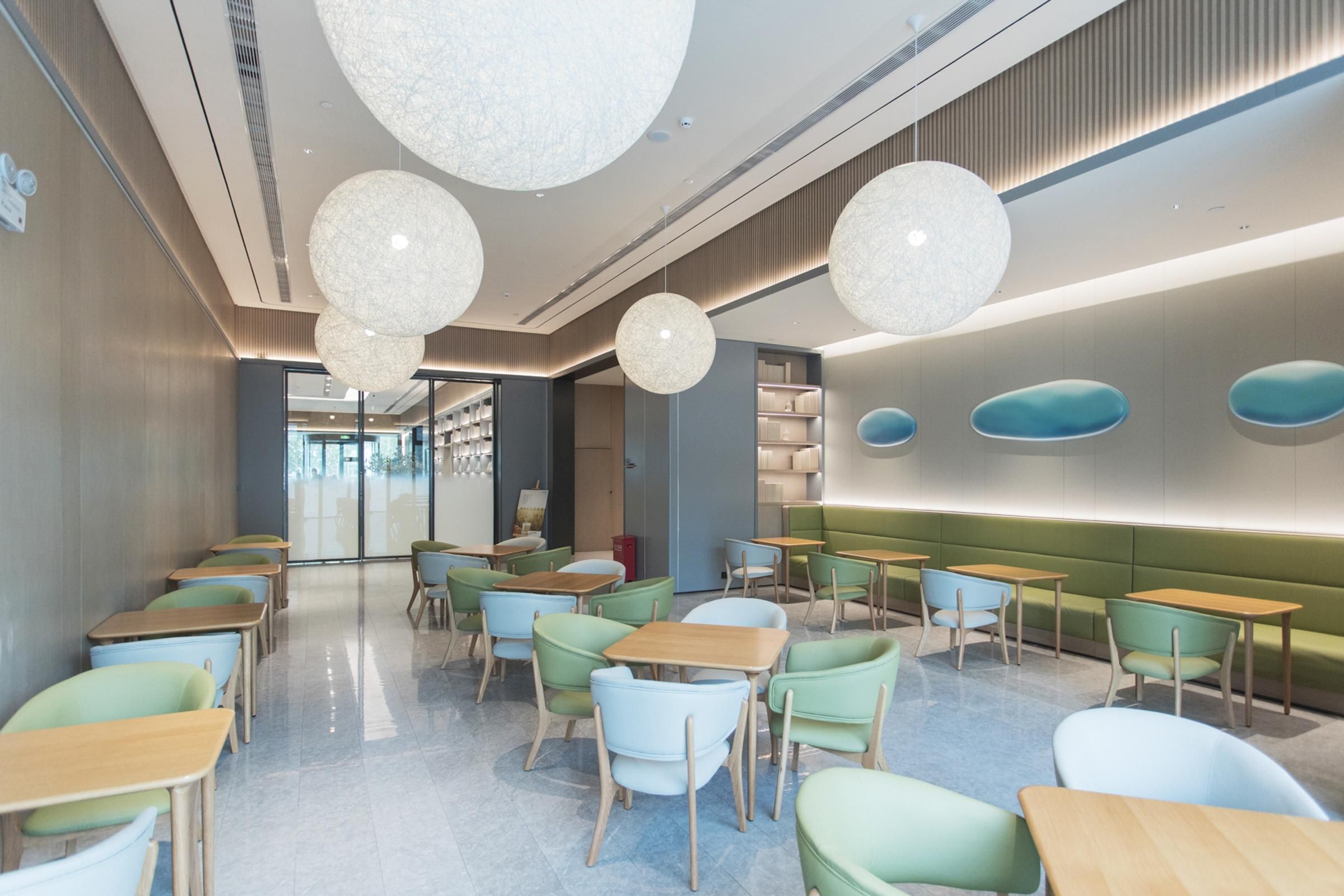 A modern interior with round chandeliers, green and blue seating, and a clean, polished floor.