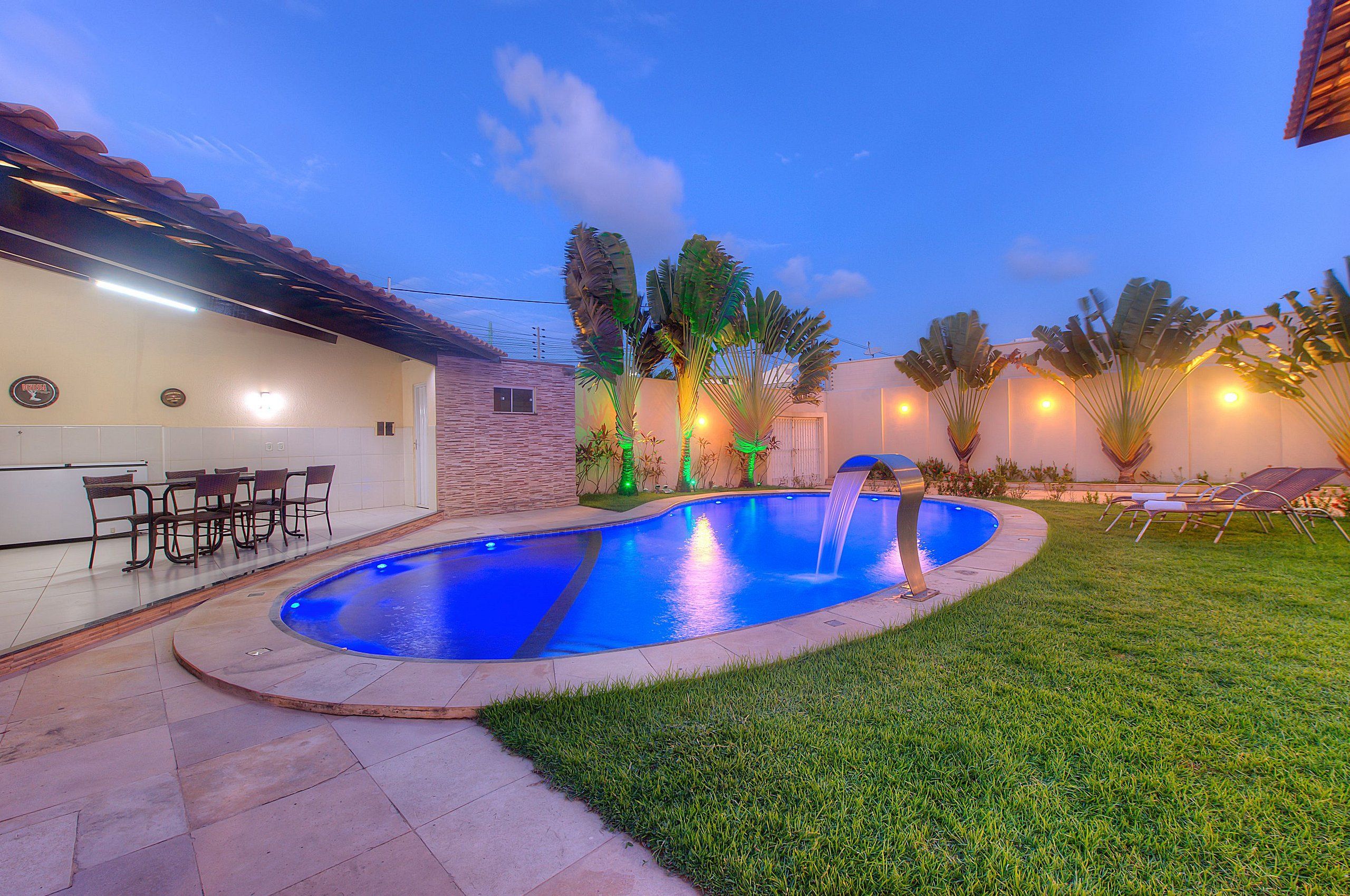 Piscina com cascata, rodeada por um jardim bem cuidado e área de estar ao ar livre.