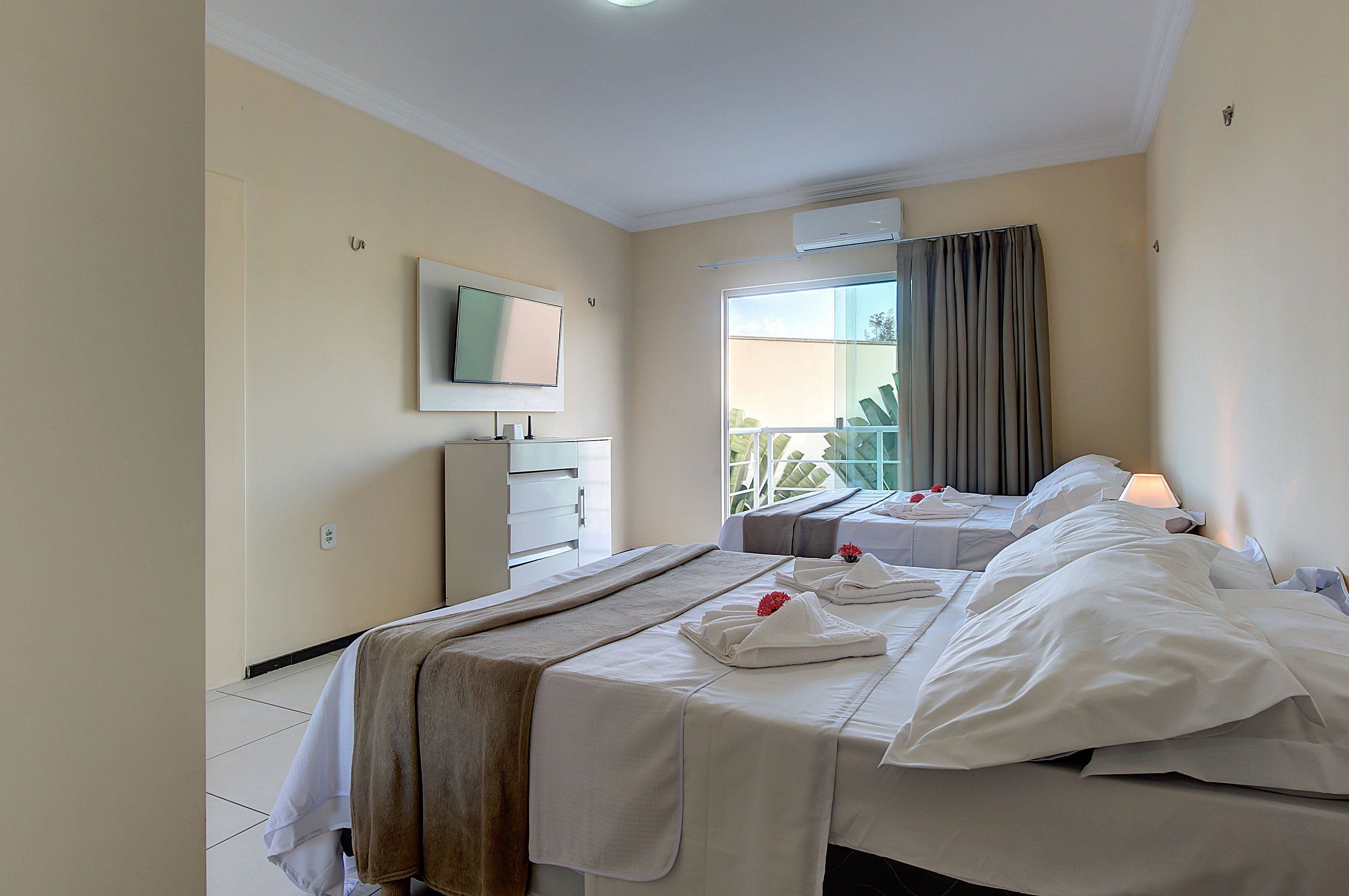 Una habitación de hotel con dos camas, un televisor, una ventana con cortinas y un balcón.