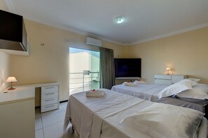 A hotel room with two beds, a desk with a lamp, a TV, and a balcony with a view.