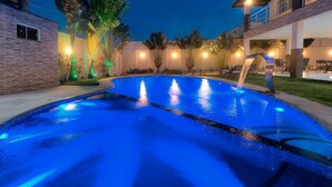 A swimming pool with a blue tint, surrounded by a modern building with a balcony and outdoor seating area. - Casa na Praia de Tabuba por Carpediem (Caucaia)