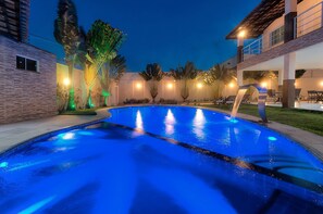 A swimming pool with a blue tint, surrounded by a modern building with a balcony and outdoor seating area. - Casa na Praia de Tabuba por Carpediem (Caucaia)