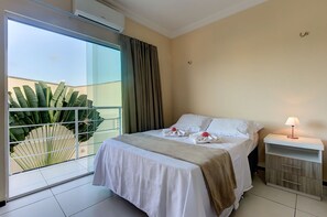 A hotel room with a bed, a nightstand, and a large window with curtains.