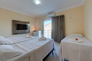 Quarto de hotel com duas camas, televisão, ar condicionado, janela com cortinas e mesa de cabeceira com abajur.
