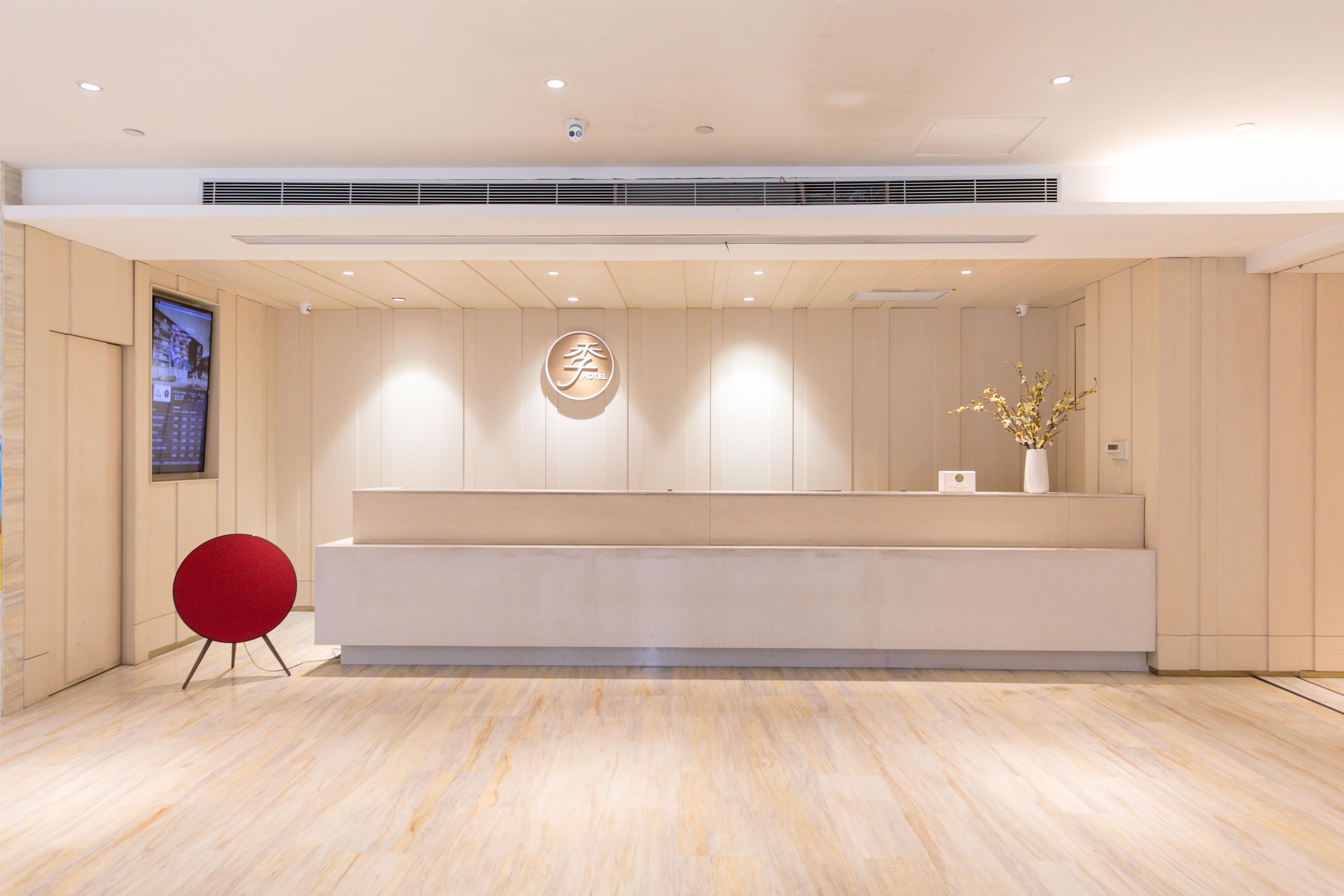A modern reception area with a wooden reception desk, a red chair, and a large digital screen on the left.