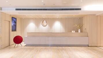A modern reception area with a wooden reception desk, a red chair, and a large digital screen on the left.