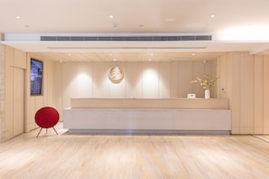 A modern reception area with a wooden reception desk, a red chair, and a large digital screen on the left. - Ji Hotel (Tongchuan)
