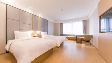 A hotel room with two beds, a desk, and a large window.