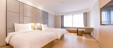 A hotel room with two beds, a desk, and a large window.