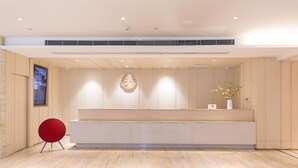 A modern reception area with a wooden reception desk, a red chair, and a large digital screen on the left. - Ji Hotel (Tongchuan)