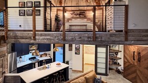Ein geräumiges Loft mit hohen Decken, einer zentralen Inselküche, einer gemütlichen Sitzecke und einem Schlafzimmer im oberen Bereich mit Blick.