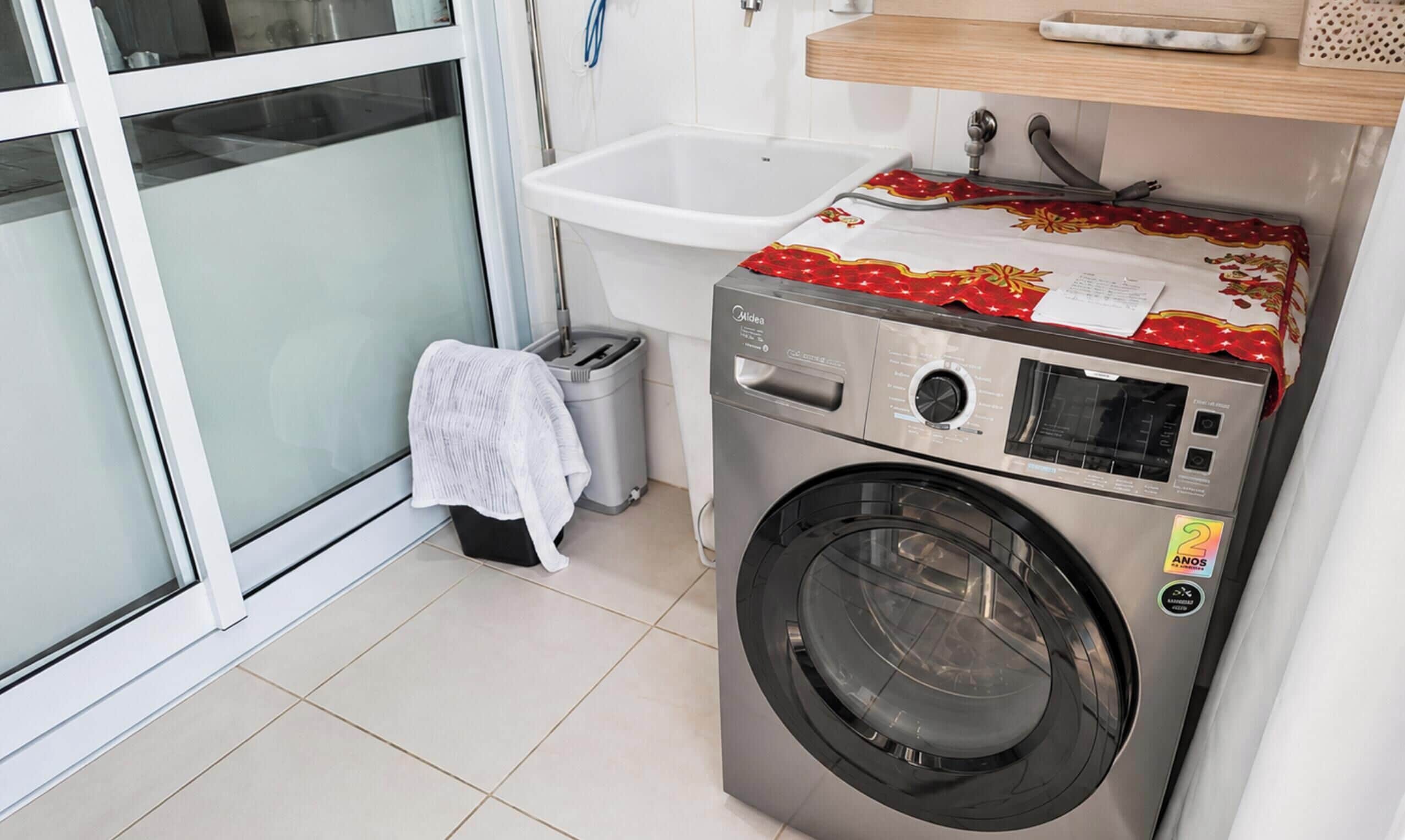 A compact laundry area with a front-loading washing machine, a small trash bin, and a white towel on the floor.