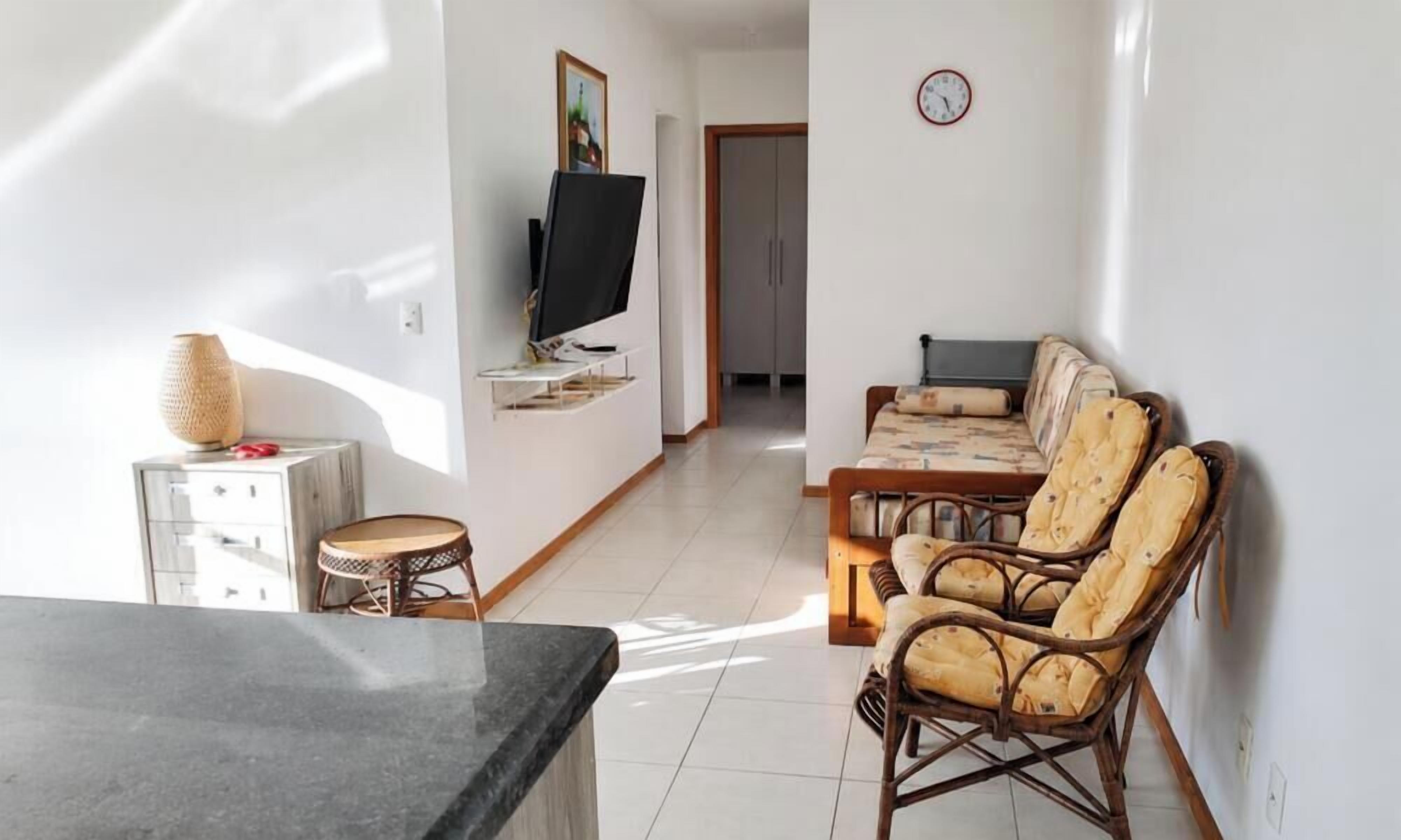 A living room with a television, wicker chairs, a sofa, a small round table, and a cabinet.