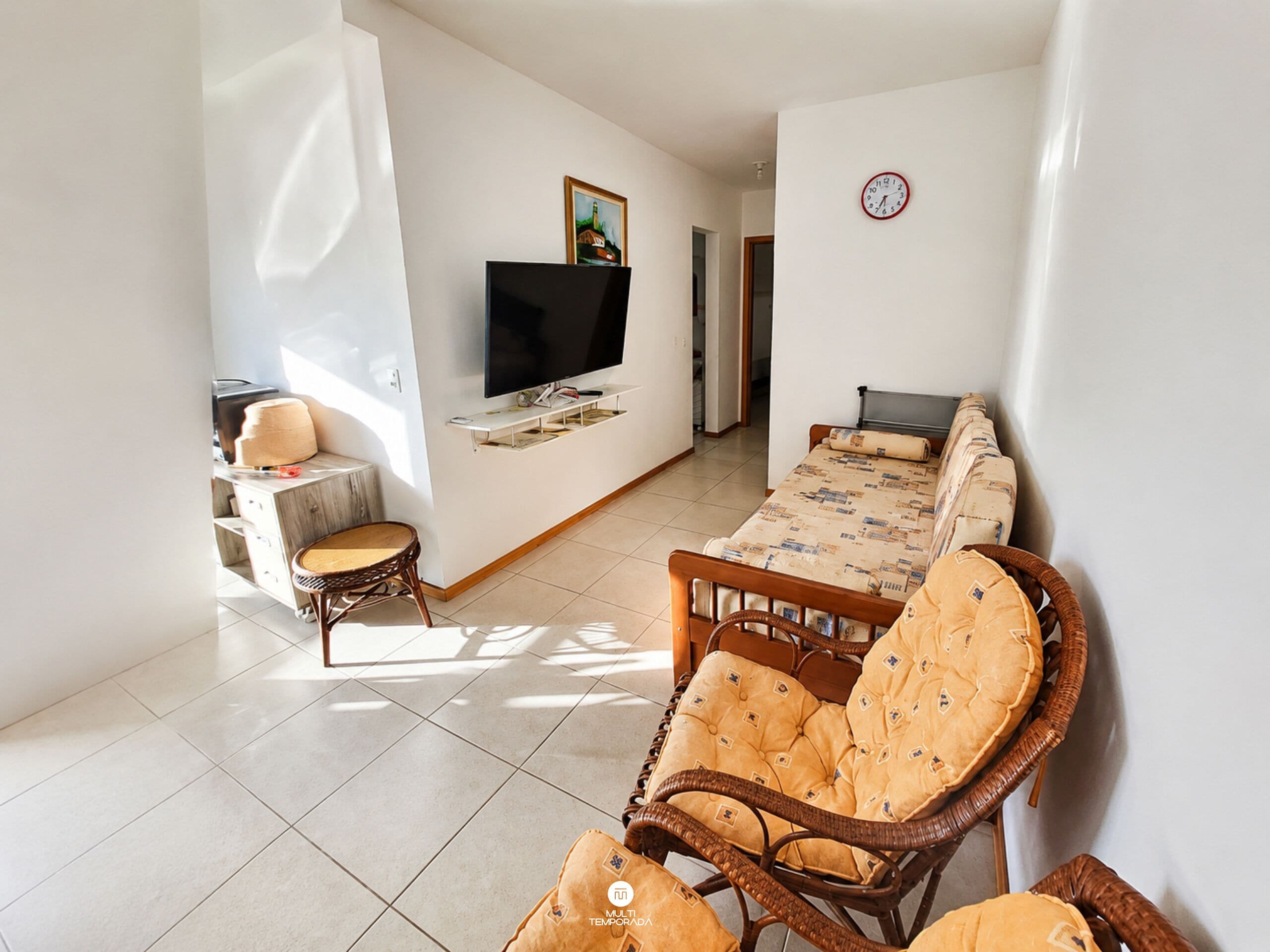 A living room with a sofa, a television, a dining table, and a wicker chair.