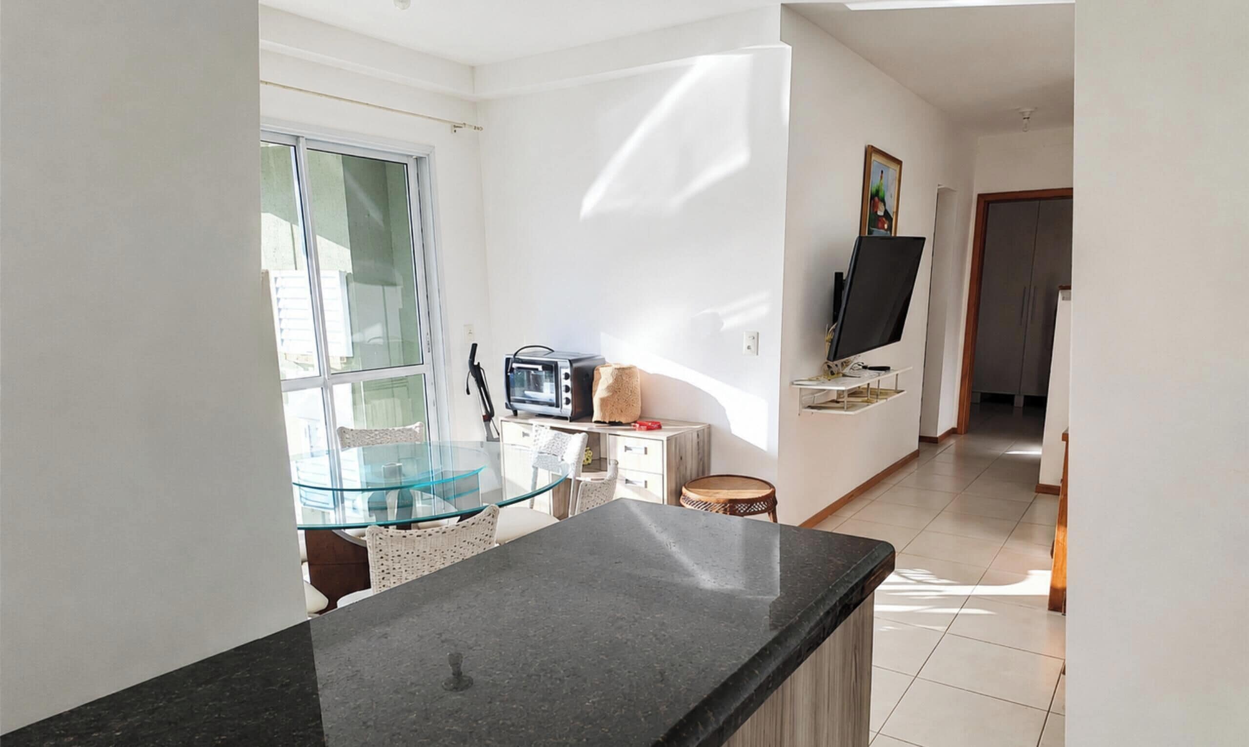 Cozinha moderna com mesa de jantar de vidro, forno embutido e televisão de tela plana em um suporte.