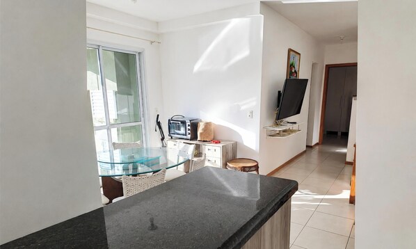 A modern kitchen with a glass dining table, a built-in oven, and a flat-screen TV on a stand. - Nautilus Ap Club Premium - Penha-SC (Penha)