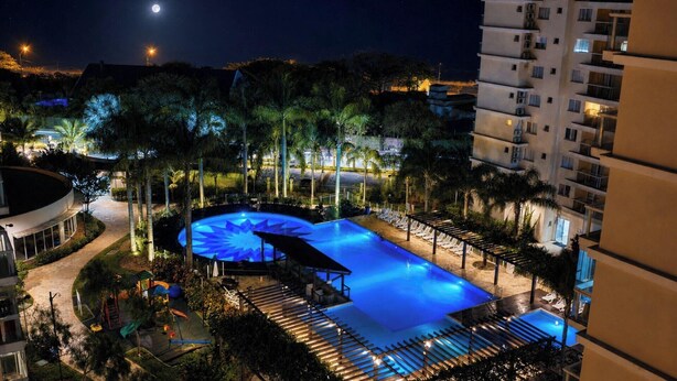 Vista nocturna de una piscina de hotel con una piscina circular, sillones de descanso y una luna creciente en el cielo.