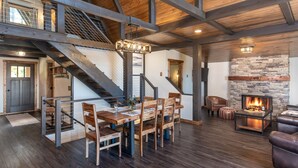 Amplia sala de estar con una mesa de comedor de madera, sillas, chimenea y una escalera.