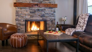 Una sala de estar acogedora con chimenea de piedra, mobiliario de cuero y una mesa con una bandeja de frutas.