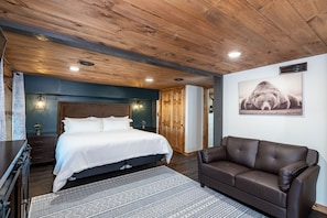 Un dormitorio con techo de madera, una cama grande, un sofá de cuero marrón y una obra de arte colgada en la pared.