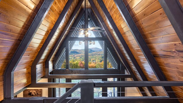 Interior de madera con techo inclinado y vista al follaje otoñal a través de una ventana.